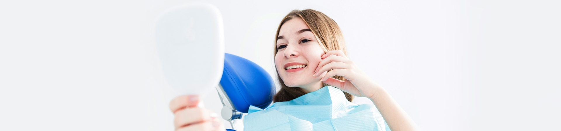 Girl checking her teeth on mirror after the dental treatment