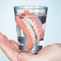 Hand holding a glass of water with dentures in it