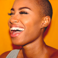 Joyful woman with a vibrant smile, close-cropped hair, against a warm yellow background.